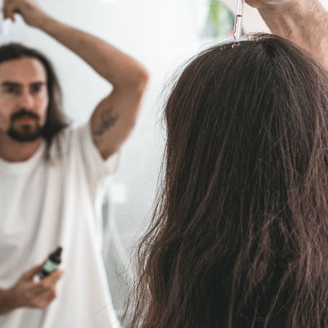 man with long hair applying hair serum
