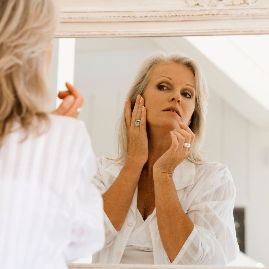 woman looking in the mirror and touching her cheek