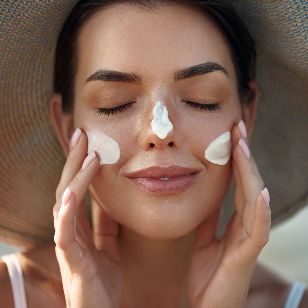 woman wearing a sun hat applying sunscreen to her face